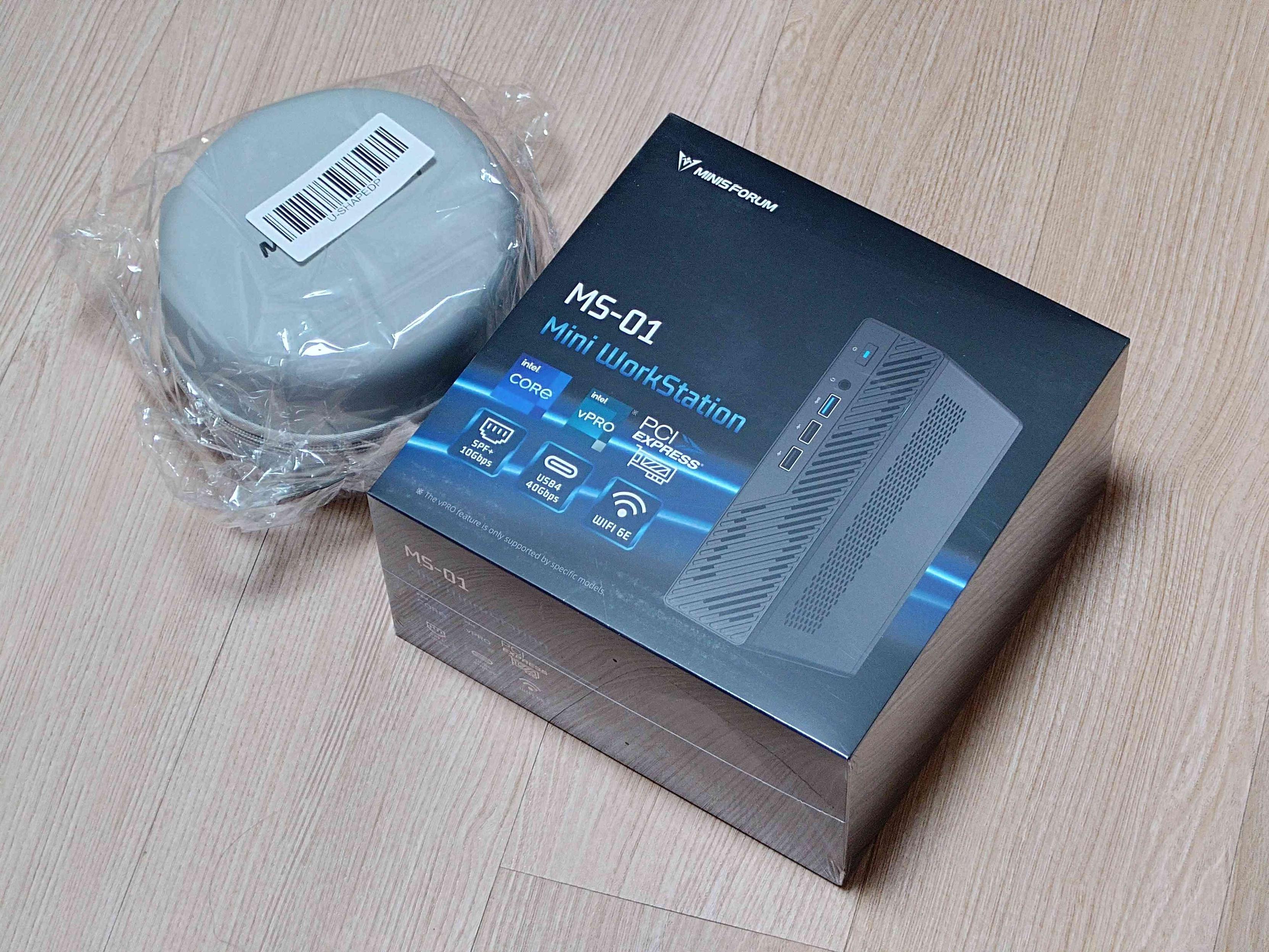 Minisforum MS-01 Intel Core Ultra 9 제품 상자와 비닐 포장된 원형 액세서리를 촬영한 사진.