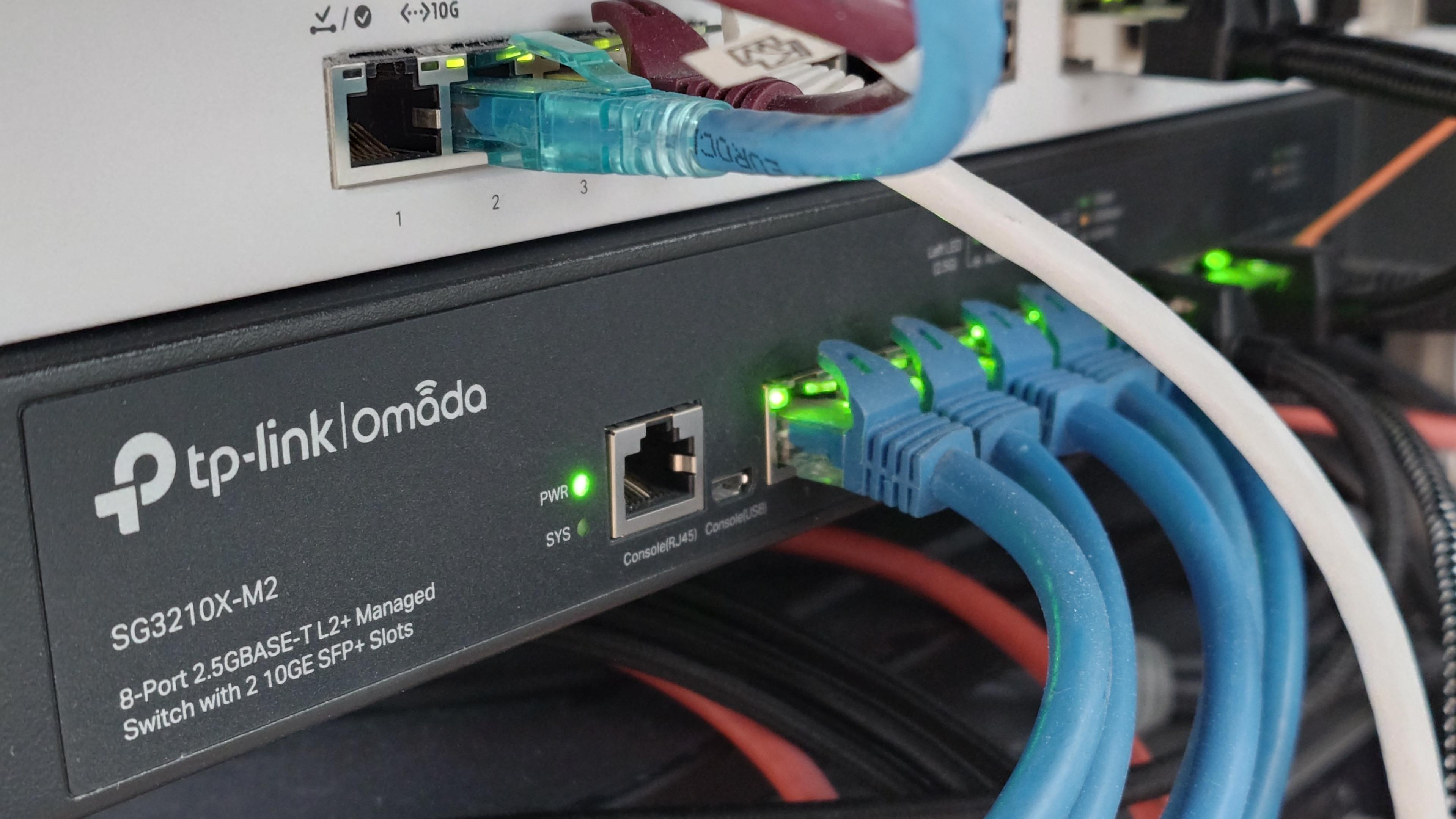 TP-Link Omada SG3210X-M2 스위치 전면 사진으로, 여러 이더넷 케이블이 연결되고 포트 LED가 켜져 있음.